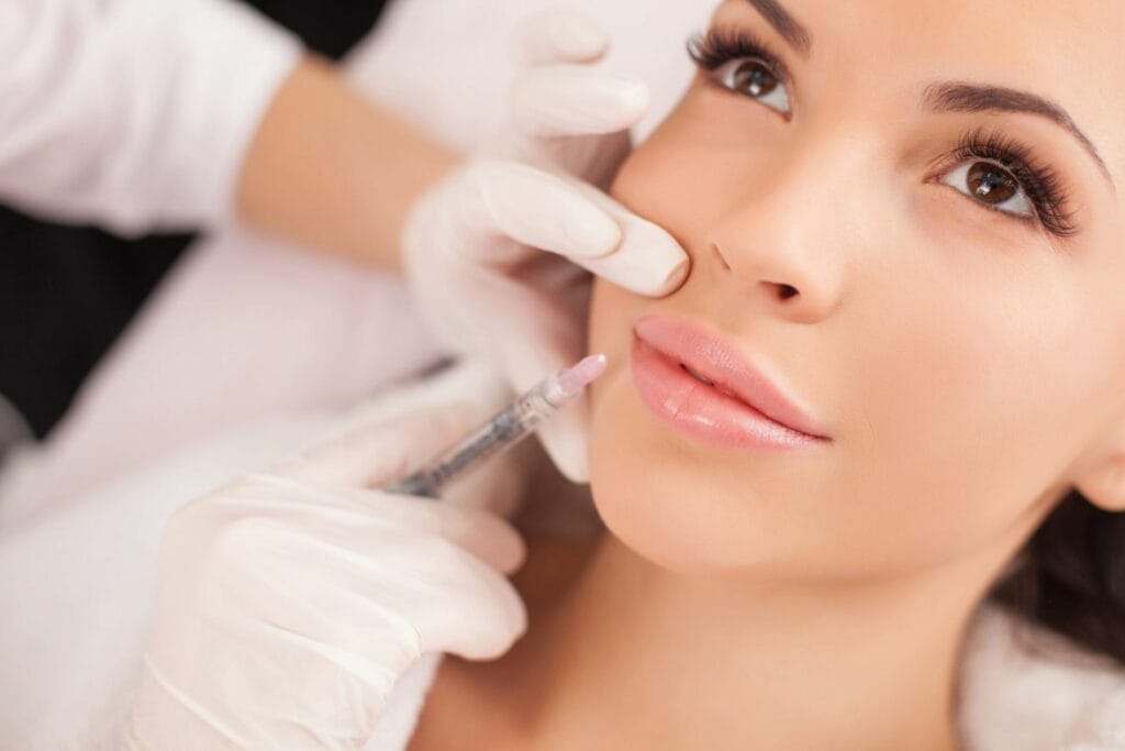 Beautiful young woman undergoing a non-surgical cosmetic procedure. Cropped sensual female lips, procedure lip augmentation. Syringe near womans mouth, injections for increase lips shape. female lips, lip augmentation procedure. A syringe near a woman's mouth, injections to increase the shape of the lips | Lily Med Spa in Dallas, Texas