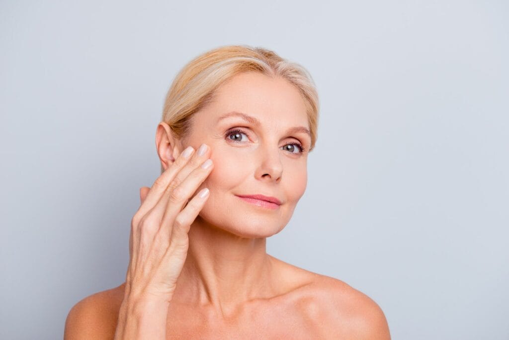 Bodycare and skincare concept. Portrait of happy adult mulatto woman with naked shoulders touching face, applying lifting cream on neck and chin isolated on white background with copy space. Adult mulatto woman isolated on white background | Lily Med Spa in Dallas, Texas