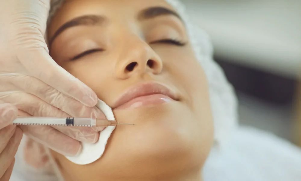 Close-up of a woman receiving chin filler injection from a professional wearing pink gloves for facial contour enhancement.